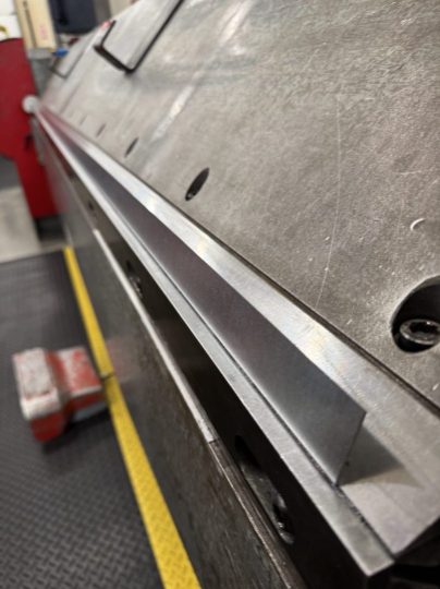 title Close-up view of a metal bending machine with a steel die and tools visible.